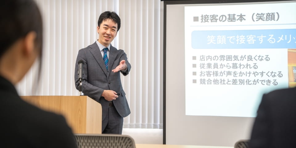 講師がプレゼン資料を使いながら新入社員に向けて研修を行っている様子